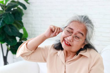 Elderly Asian women use cotton buds to wipe their earwax. The concept of health care of seniors. The danger of earwax obstruction