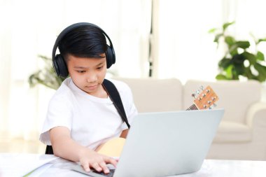 Asyalı çocuk evde online müzik eğitimi alıyor. Gitar çalma pratiği yapıyor. Müzik okulu konsepti. çocuk eğitimi