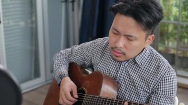 Asyalı müzisyen stüdyoda oturup gitar çalar. Müzik konsepti. online müzik dersleri