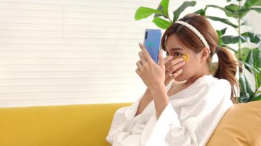 Kendine bakmak için elinde akıllı bir telefonla kaplıca yapan güzel bir Asyalı kadın altın ipek otlarla yüzünü maskeliyordu. Deriyi pürüzsüz ve güzel olması için uyarır. güzellik konsepti