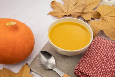 Sonbahar yapraklı kabak çorbası ve beyaz arka planda kaşık.