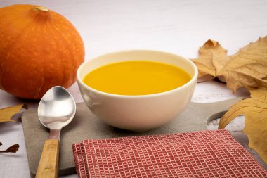 Sonbahar yapraklı kabak çorbası ve beyaz arka planda kaşık.