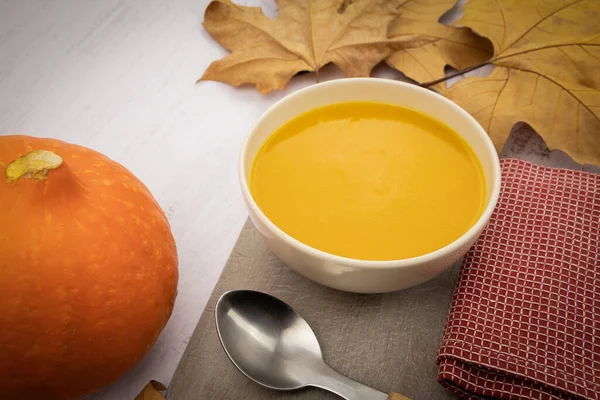Sonbahar yapraklı kabak çorbası ve beyaz arka planda kaşık.