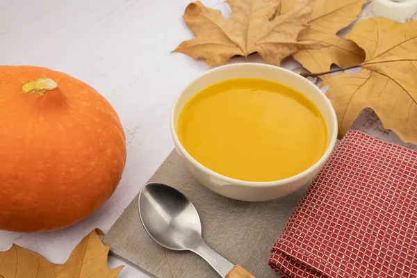 Sonbahar yapraklı kabak çorbası ve beyaz arka planda kaşık.