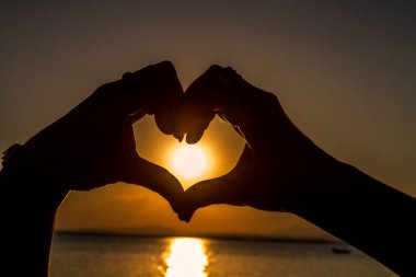 Gün batımında güzel deniz manzarasına karşı kalp şeklinde eller silueti 