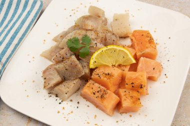 Beyaz arka planda somon ve kömür balığı kes. Masada maydanoz ve limon olsun.