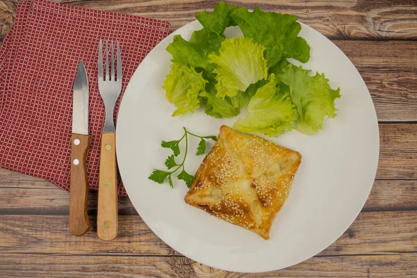 Beyaz tabakta susam tohumlu puf böreği ve salata. 