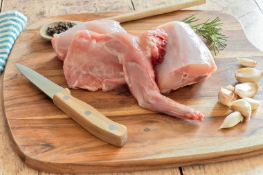 Baharatlı çiğ tavşan eti ve ahşap kesim tahtasının üzerinde otlar.