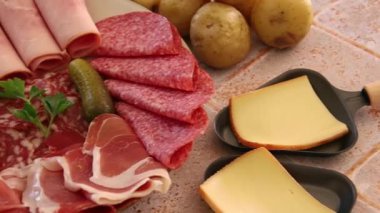 Tahtadaki raclette peyniri ve masada bir tabak jambon.