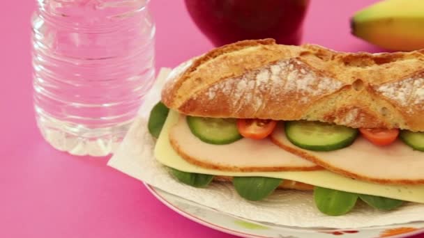 ピンクの背景にバナナとりんごのある鶏の胸肉サンドイッチ — ストック動画