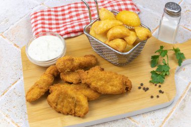 Ahşap bir tahtanın üzerinde pişmiş tavuk nugget ile patates ve sos.