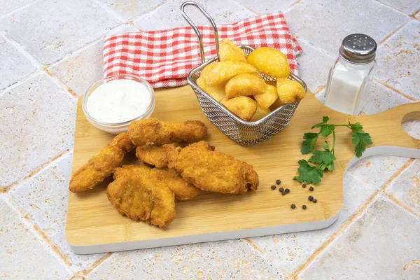 Ahşap bir tahtanın üzerinde pişmiş tavuk nugget ile patates ve sos.