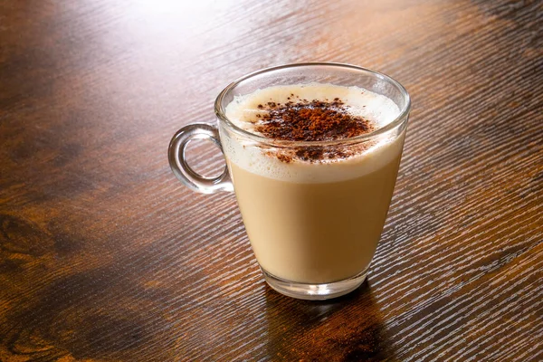 Bir bardak kapuçino kahvesi ve ahşap bir masada tarçın.