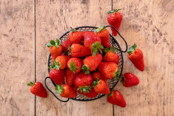 Tahta bir arka planda sepetin içinde olgun çileklerin üst görüntüsü.