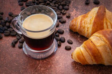 cup of coffee with roasted coffee beans and croissants on table