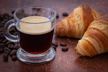 Kahve çekirdeği ve kruvasanla birlikte bir fincan kahve.