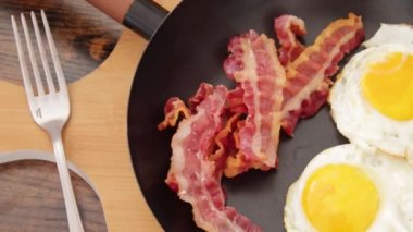 fried eggs with bacon on frying pan, toasts on table, traditional British breakfast