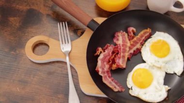 fried eggs with bacon on frying pan, beans and toasts on table, traditional British breakfast