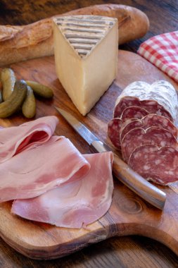 Kesme tahtasında dilimlenmiş sosis, jambon ve peynir dilimleri.