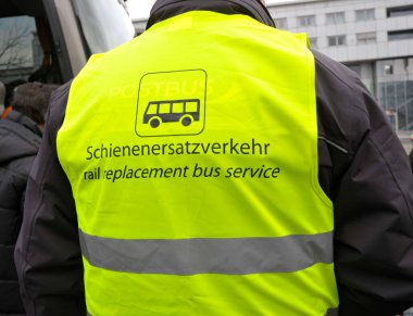 Sarı demiryolu servis tabelası, siyah harfler ve piktogram, İngilizce ve Almanca (Schienenersatzverkehr)