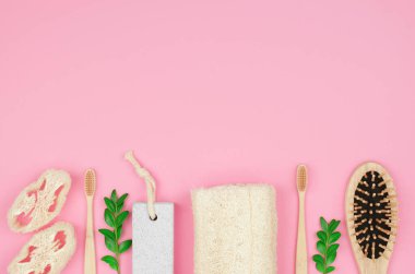 Pembe arka planda, mesaj için yeri olan çevre dostu kişisel bakım ürünleri. Bambu diş fırçaları, ahşap bir tarak ve yeşil yapraklı banyo lifleri..