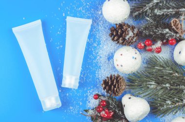 Krema tüpleri ve Noel süsü. Çam kozalakları, ağaç dalları ve kartoplarıyla kaplı kar kaplı bir masada nemlendiricinin maketi.