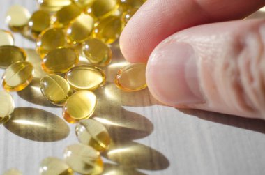 Erkek elinin yakın çekimi beyaz ahşap bir masa üzerinde D vitamini kapsülleri alır.