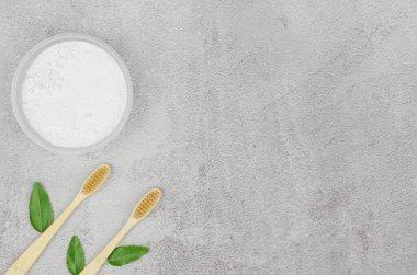 Kişisel hijyen ürünleri ekolojik konsept. Yeşil yapraklı iki ahşap diş fırçası ve yeşil yapraklı beton bir arka planda diş pudrası, kopyalama alanı