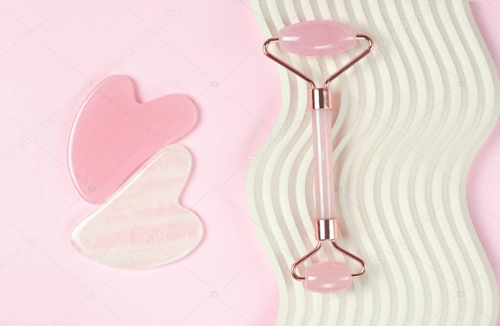 Roller jade facial massager. Gua Sha face massage tools on pink background