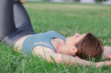 Sporcu kadın antrenmandan sonra dinleniyor. Spor giyimli güzel bir kadın çimlerin üzerinde yatıyor.