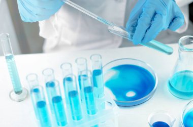 Bilim adamı koronavirüse karşı bir aşı üzerinde araştırma yapıyor. Laboratuvar klinik deneyleri. Bilim adamının elleri bir matara ve laboratuvar pipetini tutuyor.