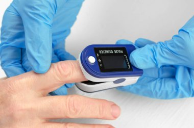 60 yaşında bir kadında doygunluk ölçüsü var. Tıbbi eldivenli bir doktorun elleri yaşlı bir kadının parmağına nabız oksimetresi uyguluyor. Yaşlıların sağlığıyla ilgilenmek.