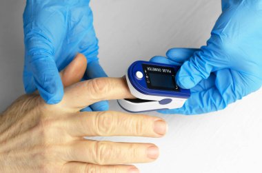 60 yaşındaki Asyalı bir kadının doygunluk ölçümü. Tıbbi eldivenli bir doktorun elleri yaşlı bir kadının parmağına nabız oksimetresi uyguluyor. Yaşlıların sağlığıyla ilgilenmek.