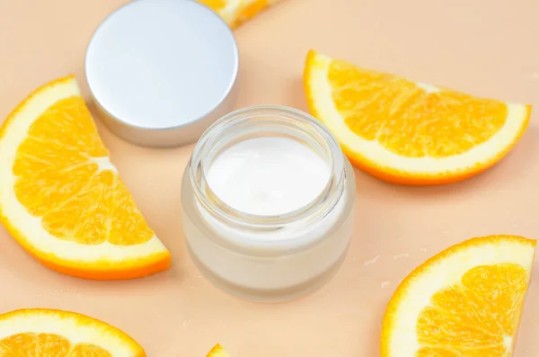Moisturizing cream with orange extract. Open jar of cream and orange slices on beige background