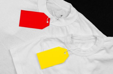 Two white t-shirts on a black background with empty price tags. Blank label on clothes