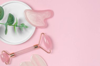 Jade face massager and gua sha massage scraper on wave podium, copy space. Facial skin care products