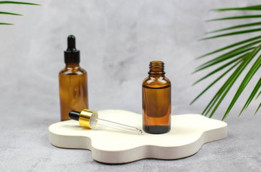 Beyaz kıvrımlı bir kürsüde bir şişe yağlı boya duruyor. Doğal cilt bakımı kavramı. Doğal bitkisel ürünler. Gri arka planda kozmetik pipeti