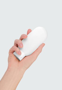 Kadının eli gri arka planda izole edilmiş beyaz kozmetik tüpü tutuyor. Kozmetik marka modeli. Cilt bakımı kavramı