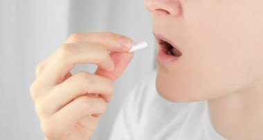 Ağzına hap koyan bir kadının yakın çekimi. Tanımlanamayan bir kadın antipiretik ya da ağrı kesici içiyor.