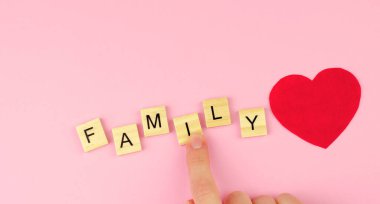 Ahşap harflerden aile ve pembe arka planda kırmızı bir kalp. Kadın eli aile ve ahşap harfleri toplar.