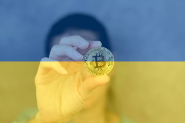 Ukrayna bayrağının arka planına yakın plan çekilmiş bir kadın eli Bitcoin. Ukrayna 'da kripto para birimi