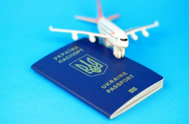 Mavi arka planda Ukrayna pasaportu ve bulanık oyuncak uçağı, seçici odaklı