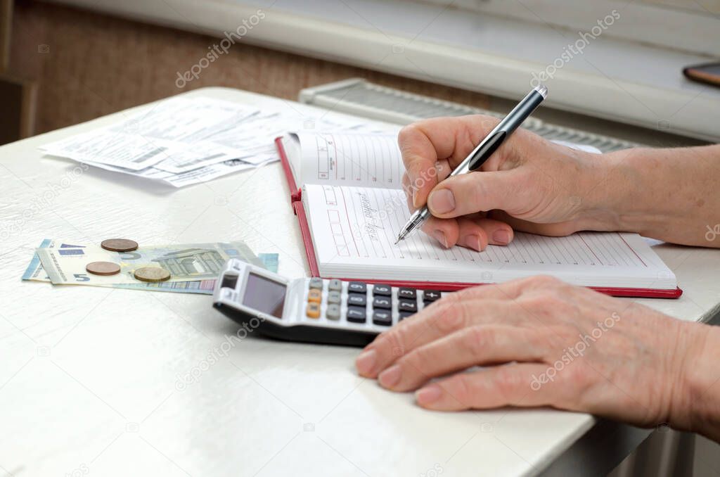 Close-up of an elderly woman's hands holding a pen working on a utility bill calculator.