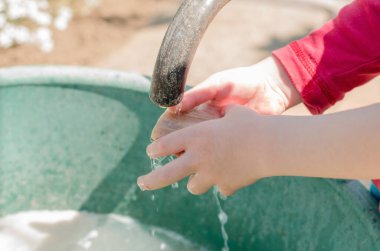 Çocuk ellerini yıkıyor, yakın plan. Avludaki musluğun altındaki çocuğun ellerini yakın plan çek.