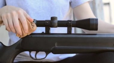 Dişi bir keskin nişancı tüfeğinin optik görüş açısını temizliyor, yakın plan. Kadınların elleri, havasız bir tüfeğin tozunu alır.