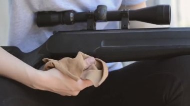 Dişi bir keskin nişancı tüfeğinin optik görüş açısını temizliyor, yakın plan. Kadınların elleri, havasız bir tüfeğin tozunu alır.