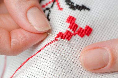 Bir kadın Ukrayna 'nın ulusal sembollerini haçla işliyor. Beyaz tuval üzerinde çapraz dikiş atan kadın ellerinin yakın çekimi.