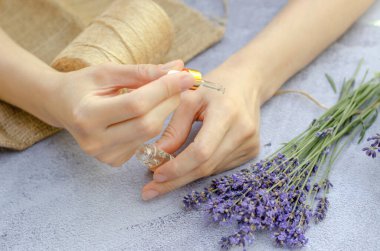 Dişi eller lavanta yağlı pipeti tutuyor. Ellerindeki pipetten damlayan lavanta yağı, yakın plan.