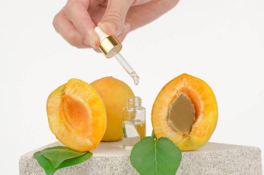 Kadın elinde kayısı yağı olan bir pipo. Kozmetik şişesi, yüz serumu ve taze kayısılar.