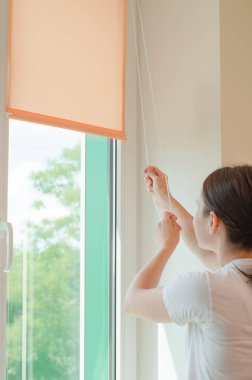 Woman lowers or raises roller blinds in her office